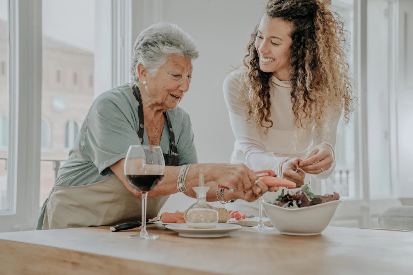 A caregiver and an older woman cooking together in a bright kitchen